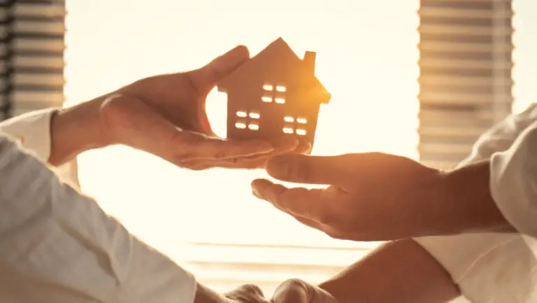 Holzhaus wird symbolisch für ein richtiges Haus von Hand zu Hand übergeben