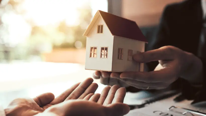 Holzhaus wird symbolisch für ein richtiges Haus von Hand zu Hand übergeben