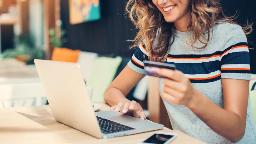 Junge Frau, die an einem Laptop mit einer Kreditkarte sitzt