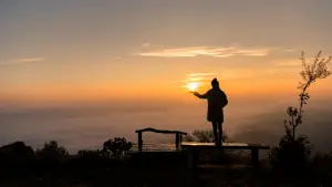 Mensch steht vor einem Sonnenaufgang und hält die Sonne vermeintlich in der Hand