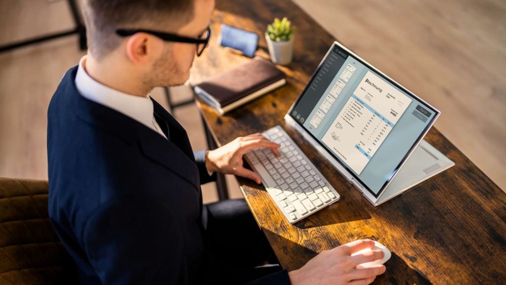 Junger Mann sitzt vor einem Tablet und stellt eine E-Rechnung aus.